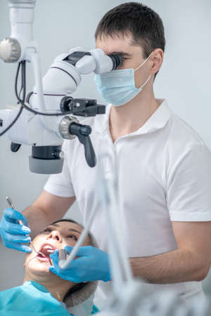 Male dental surgeon working with patient and using optical medical instrumentの写真素材