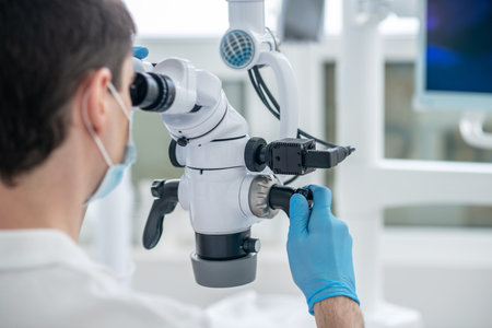 Male dentist working using optical medical instrument while doing a dental restoration