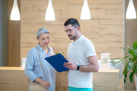 Mature good-looking woman talking to the doctor at the reception and looking involvedの写真素材