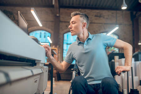 Attentive man in wheelchair near copy machine at work