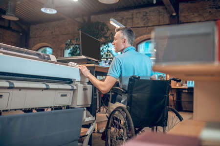 Young adult man in wheelchair operating copierの写真素材