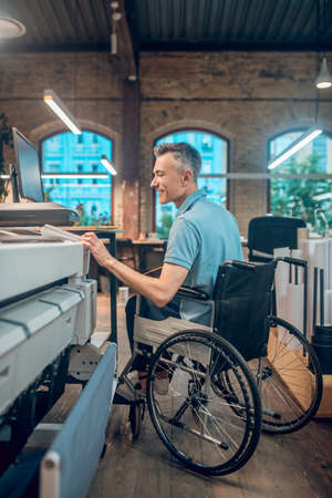 Smiling disabled man at workplace near copy machineの写真素材