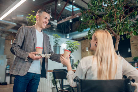 Man giving glass of coffee to woman in wheelchairの写真素材
