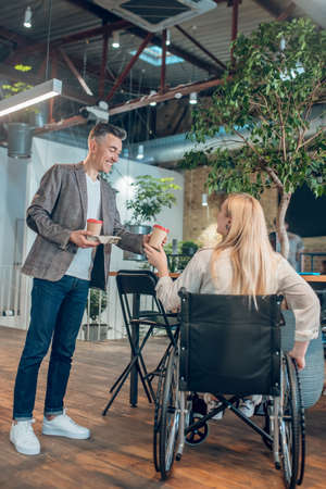 Man standing with coffee and woman in wheelchairの写真素材