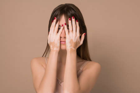 A young pretty long-haired woman with skin pigmentation closing her face with her handsの写真素材