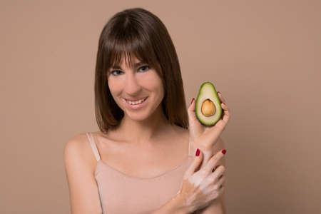 A slim long-haired woman in beige lingerie with avocado in her handsの写真素材