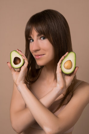 A slim long-haired woman in beige lingerie holding avocadoの写真素材