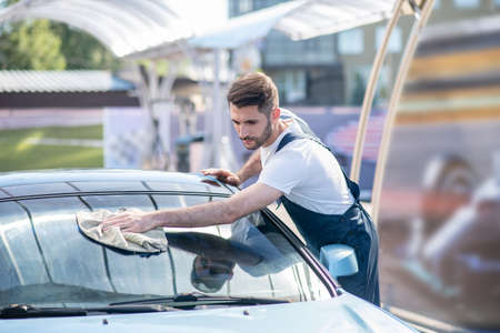 Man in work clothes wiping glass of carの写真素材