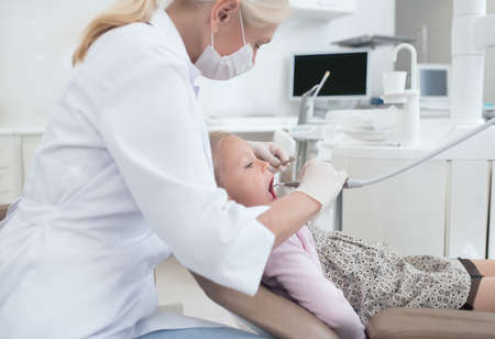 Teeth treatment. A blonde doctor in a white robe working with a little patientの写真素材