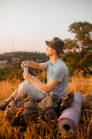 A man in a hat sitting on the hill and opening his flaskの写真素材