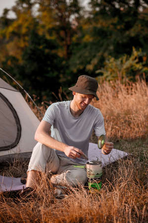 A male tourist sitting near the tent and getting his food ready