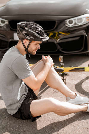 Young man sitting near fallen bikeの写真素材