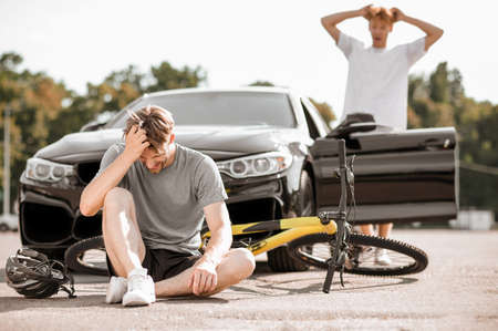 Injured cyclist on the road and driverの写真素材