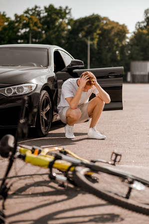 Desperate guy crouched near car after accidentの写真素材