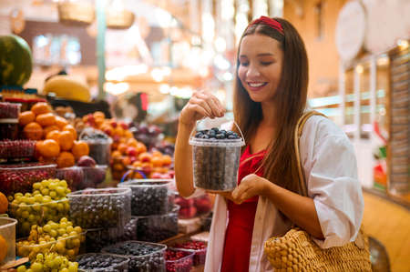 Cute woman buying berries and looking excitedの写真素材