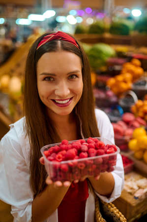 Cute woman choosing berries in a fruits store and looking excitedの写真素材