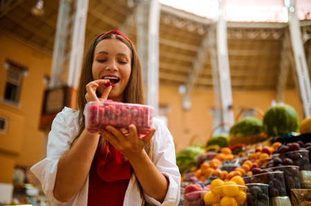 Cute woman choosing berries in a fruits store and looking excitedの写真素材