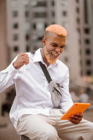 A picture of a man with dyed hair with a tablet in handsの写真素材