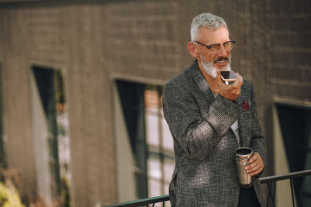 A gray-haired man in eyeglasses recording an audio messageの写真素材