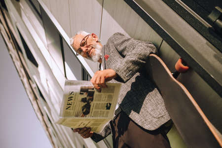 A gray-haired businessman reading a newspaper and looking concentratedの写真素材