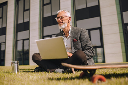 Pensive handsome man with notebook computer sitting outdoorsの写真素材