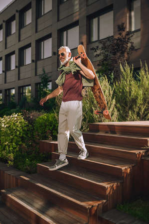 Cheerful skateboarder in sunglasses going down the wooden stairsの写真素材