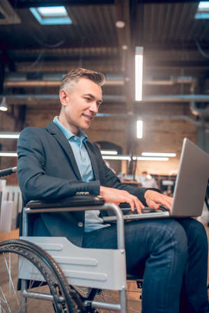 Man in wheelchair holding laptop on lap and workingの写真素材