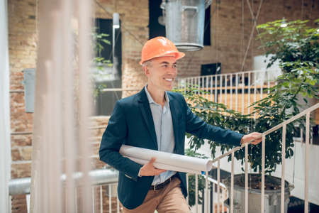 Man in helmet with blueprints smiling looking to sideの写真素材