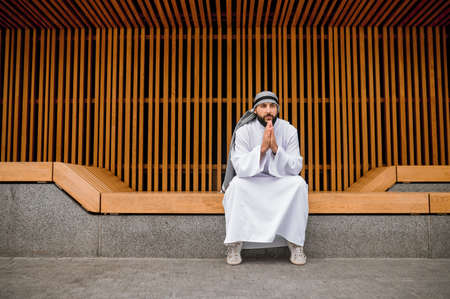 Middle eastern young man in traditional clothing sitting on a wooden benchの写真素材