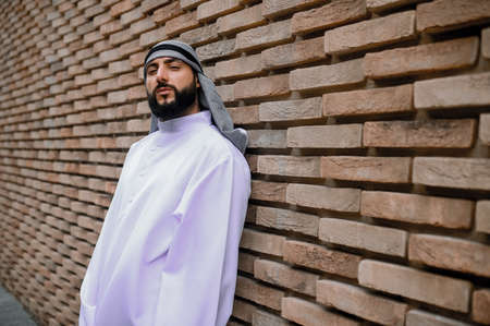A man in traditional arabian headwear standing near the brick wallの写真素材