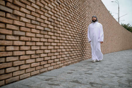 A man in traditional arabian headwear standing near the brick wall