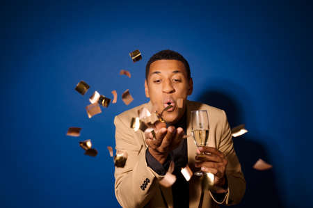 Guy with champagne blowing on hand with confettiの写真素材