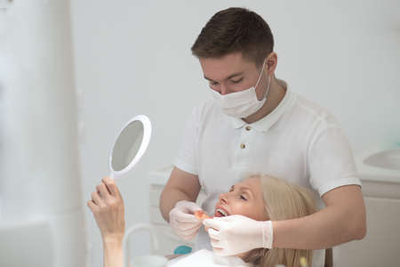 A female patient looking in the mirror at the results of the dental surgeryの写真素材
