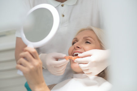 A female patient looking in the mirror at the results of the dental surgeryの写真素材
