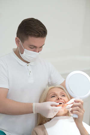 A female patient looking in the mirror at the results of the dental surgeryの写真素材