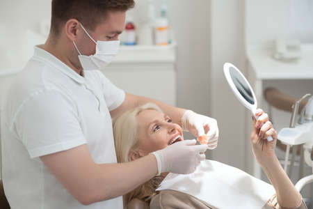 A female patient looking in the mirror at the results of the dental surgeryの写真素材