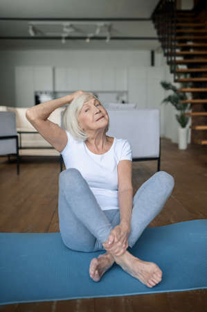 Senior woman sitting on a mat and doing exercises