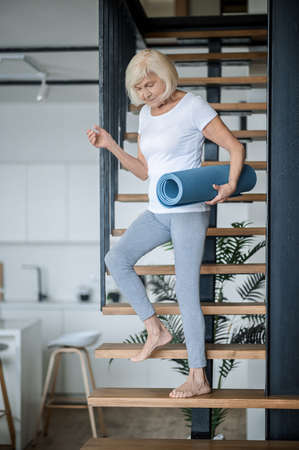 A senior woman getting downstairs with a yoga mat in handsの写真素材