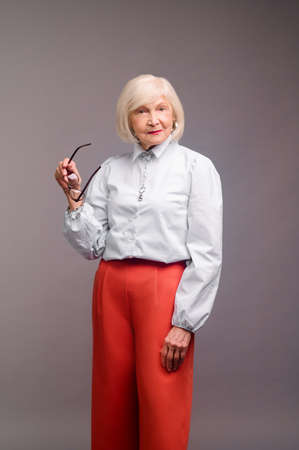 Elegant senior woman in white blouse and red pantsの写真素材