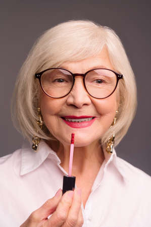 Blonde stylish senior woman putting lip gloss on her lipsの写真素材