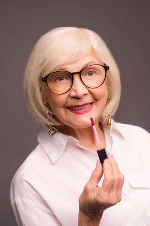 Blonde stylish senior woman putting lip gloss on her lipsの写真素材