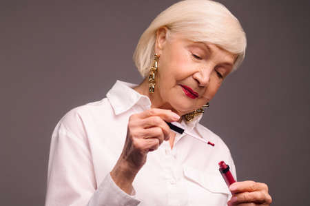 Blonde senior woman holding a red lipstick and looking contentedの写真素材