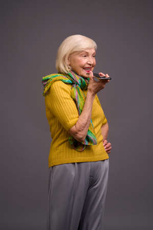 Senior woman in yellow shirt and with a green scarf recording a voice messageの写真素材