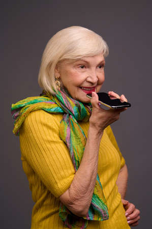 Senior woman in yellow shirt and with a green scarf recording a voice messageの写真素材