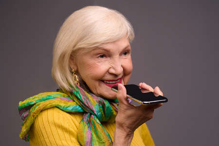 Senior woman in yellow shirt and with a green scarf recording a voice messageの写真素材