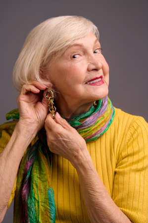 Blone smiling senior woman putting on long earringsの写真素材