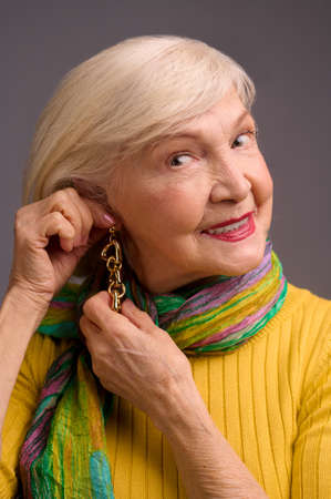 Blone smiling senior woman putting on long earringsの写真素材