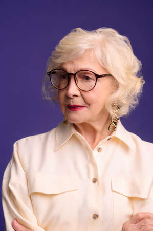 Elegant senior lady in eyeglasses in beige shirtの写真素材