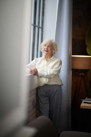 Thoughtful woman standing looking out windowの写真素材