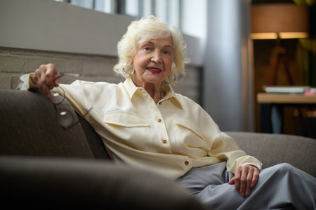 Woman looking at camera sitting on sofa near windowの写真素材